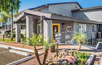 a building with a yellow door and a porch with palm trees in front of it