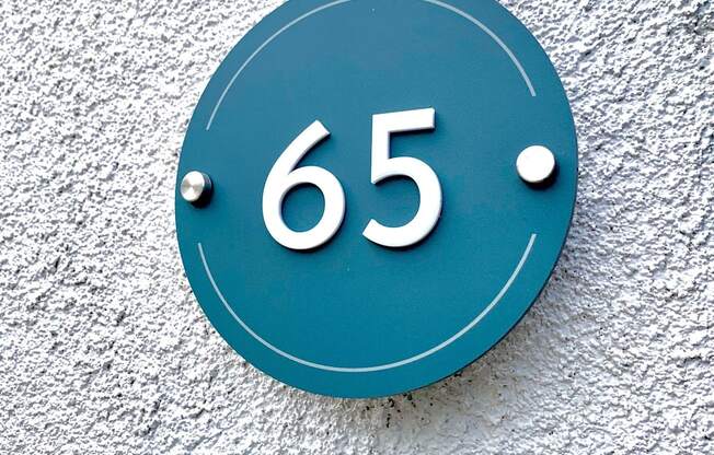 a blue sign with the number 65 on a white wall