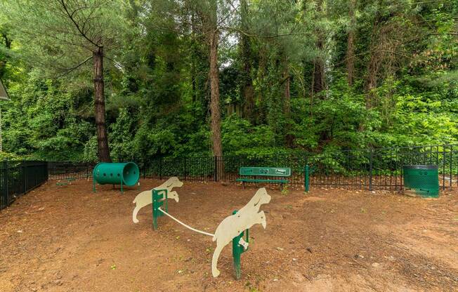 A dog park with two wooden dog sculptures and a green trash can.
