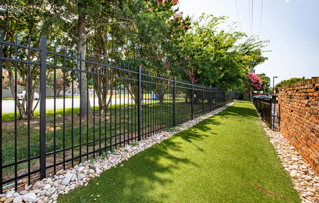 a black wrought iron fence in front of a green lawn and trees