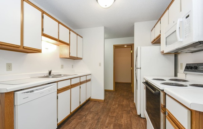 a kitchen with white appliances and wood flooring and white cabinets. Anoka, MN Dellwood Estates