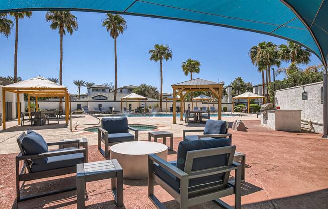 a patio with chairs and tables and a pool with palm trees in the background