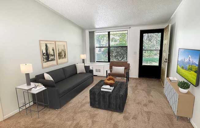 A living room with a black couch, a small table, and a painting on the wall.