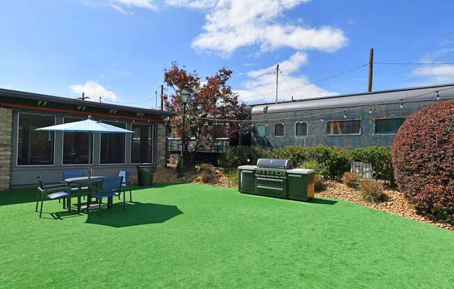 A green lawn with a table and chairs and a tree.