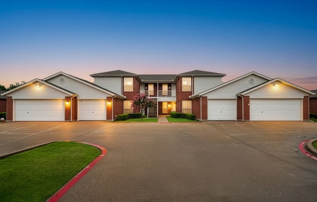 A row of houses with garages are shown at dusk.