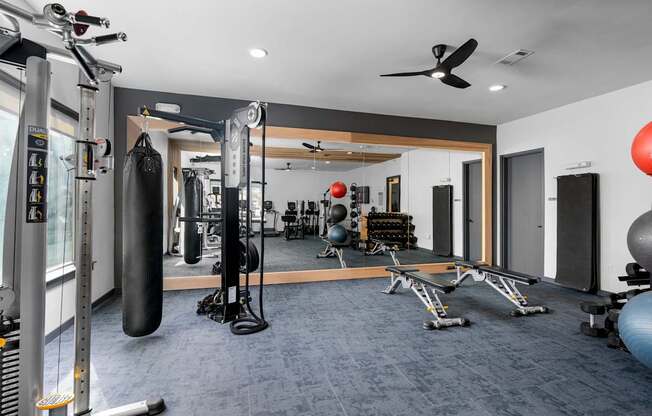 A gym with a variety of equipment including a punching bag, weight bench, and exercise balls.