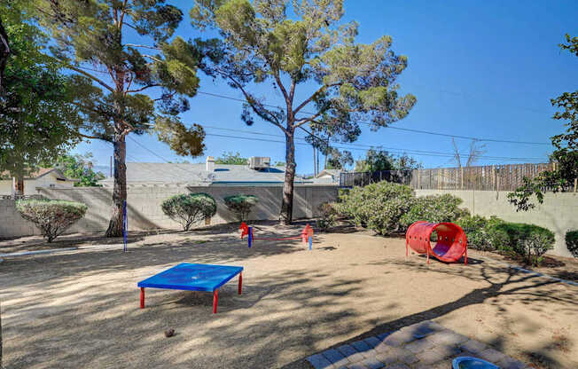 A backyard with a blue trampoline and a red tunnel.