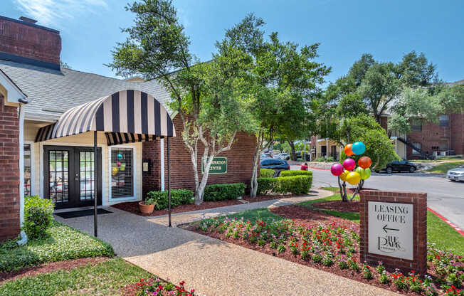 A leasing office is located in a landscaped area with a striped awning.