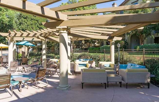 A patio with a white couch and chairs under a wooden pergola.