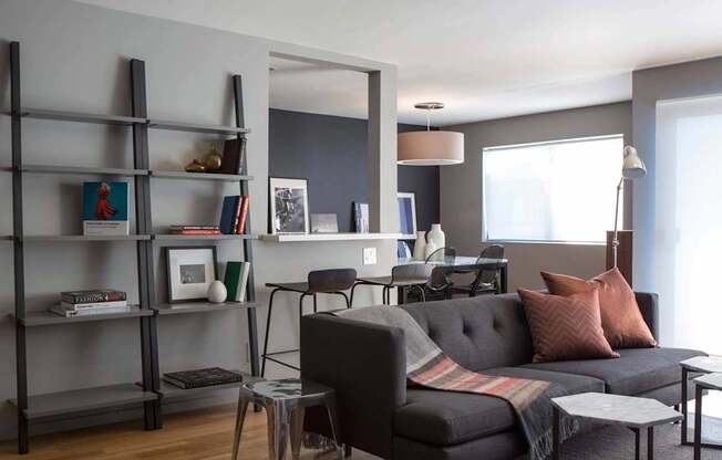 A living room with a grey couch, a chair, a table, and a bookshelf.