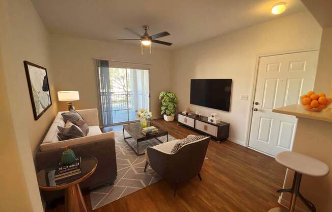 A living room with a brown sofa, a white armchair, a coffee table, a television, and a ceiling fan.