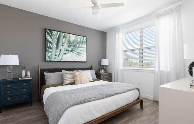 a bedroom with a ceiling fan, large window, wood-style floors, and model furnishings