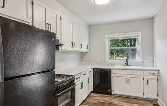 A black refrigerator in a kitchen with white cabinets and a window.