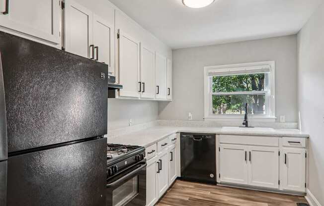 A black refrigerator in a kitchen with white cabinets and a window.