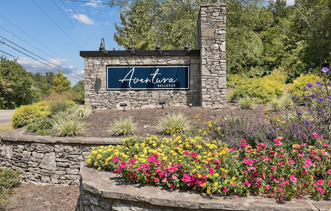 A stone wall with a sign that says Aventura in front of a field of flowers.