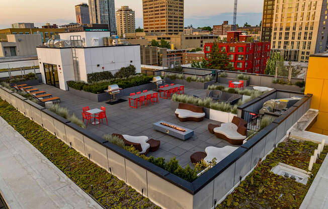 A rooftop patio with red chairs and tables overlooks a city skyline.