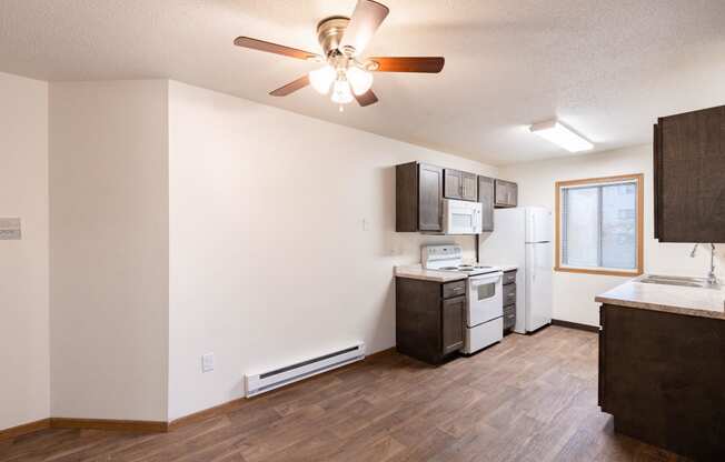 an empty living room with a kitchen and a ceiling fan. Fargo, ND Oxford Apartments