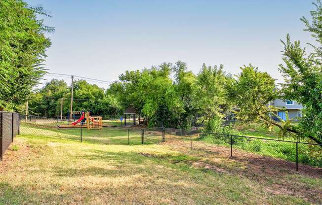 the yard is fenced in with a playground and trees