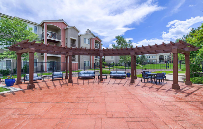 A red brick patio with a pergola and benches in front of apartment buildings.