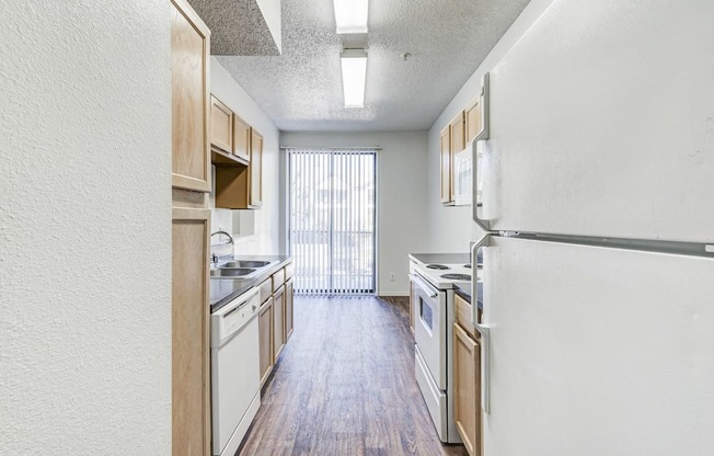 A bright dining area at Saxony at Chase Oaks Apartments in Dallas, TX, with wood-style flooring, a sliding glass door with vertical blinds, and neutral-colored walls.