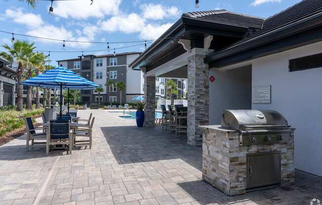 A patio with a grill and chairs under a blue umbrella.