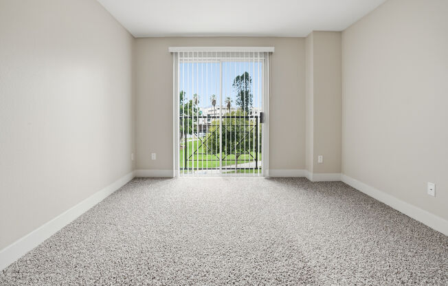 A room with a carpeted floor and a sliding glass door leading to a backyard.