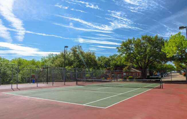 Tennis court with trees surrounding the court at Chisholm Place Apartments in Plano, TX