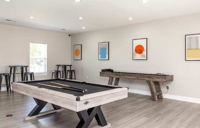 A pool table is in the middle of a room with a white wall and a window.