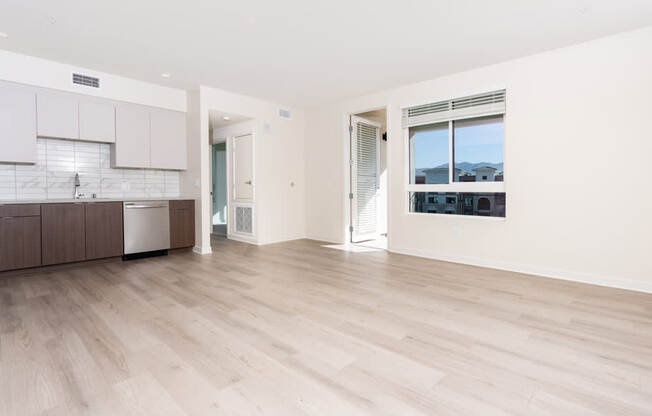 A spacious room with wooden flooring and a view of buildings outside the window.