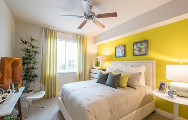 Model bedroom at our apartments in Miami, featuring yellow walls, white bedspread, and a large window.