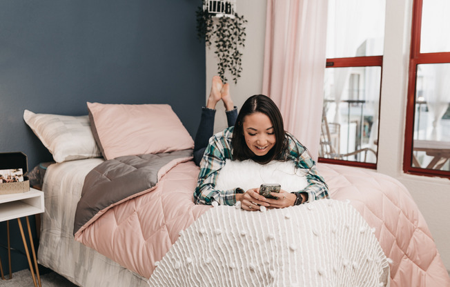 Young woman on a bed, on her phone smiling