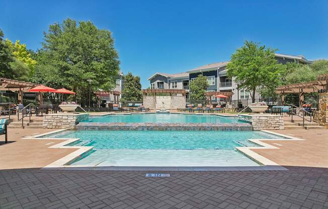 A large outdoor swimming pool surrounded by a stone wall and seating areas.