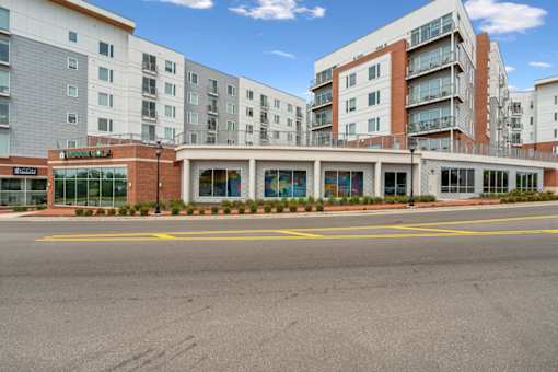 A large building with a glass entrance and a red brick base at The Waterford At Rocketts Landing Apartments, PRG Real Estate, Richmond, Virginia