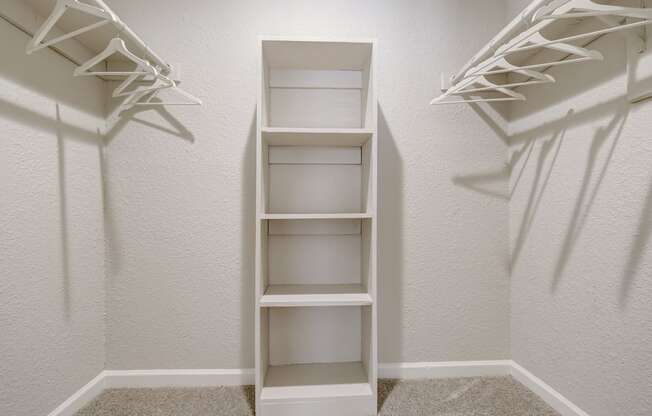 a walk in closet in a bedroom with white shelves and white walls
