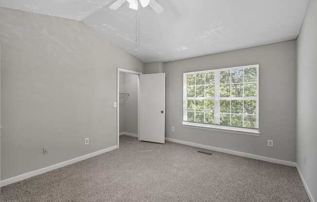 A room with a carpeted floor, a window with a view of trees, and a white door.