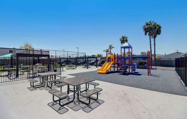A playground with a yellow slide and picnic tables.