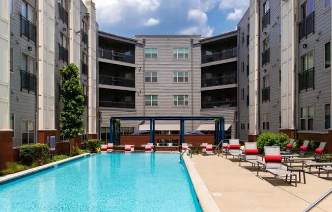 A swimming pool in front of a building with red lounge chairs.
