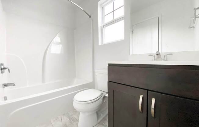 A white toilet sits in a bathroom next to a bathtub and a sink.