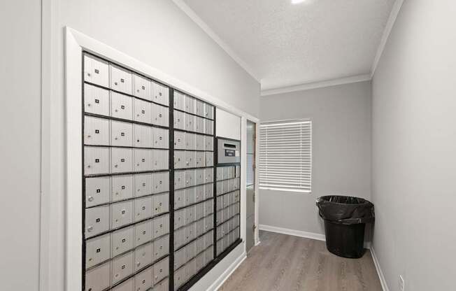 A room with a wall of mailboxes and a trash can.