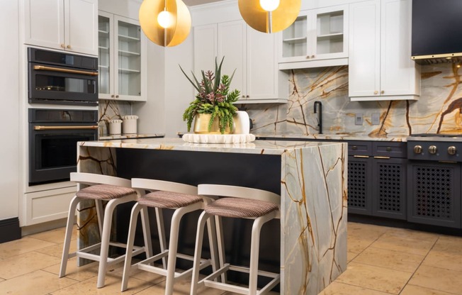 a kitchen with white cabinets and a marble island with three bar stools