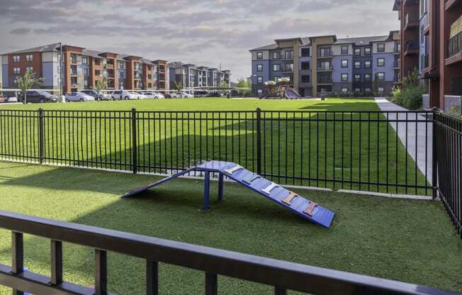 a blue slide sits in the middle of a grassy area in front of an apartment complex