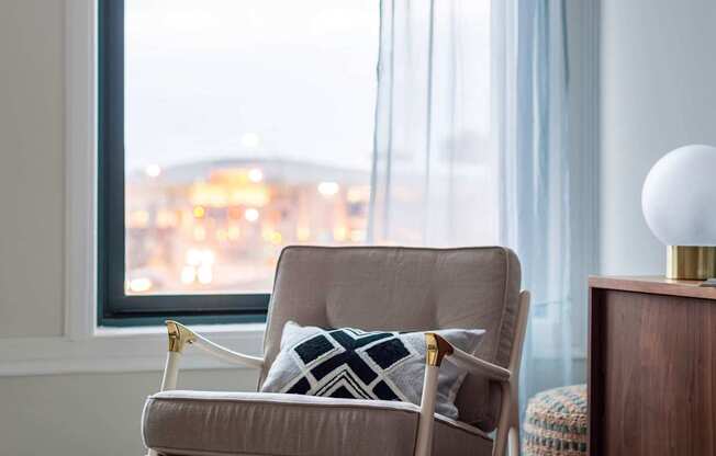 A chair with a cushion and a pillow is in front of a window at The Pennsylvanian Apartments, Pittsburgh