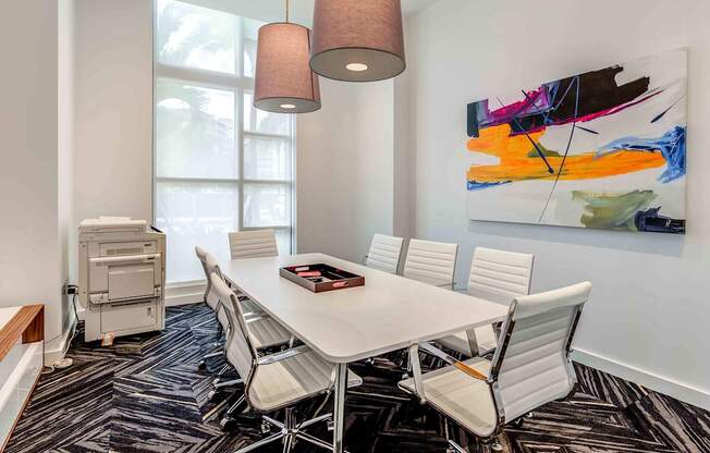 A conference room with a white table and chairs, a large abstract painting on the wall, and a floor lamp.