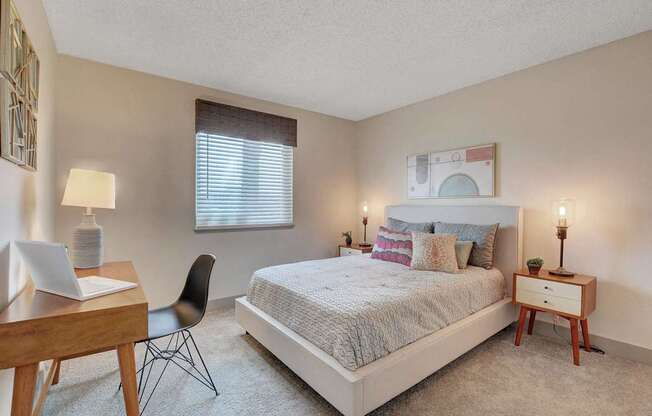 A bedroom with a bed, desk, chair, and window.