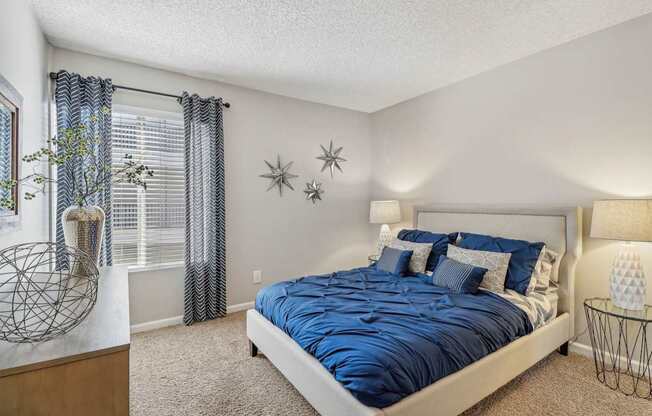 A bedroom with a bed, nightstand, and a window with curtains.