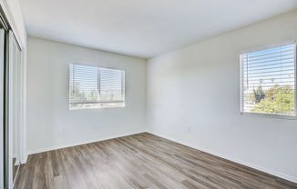 an empty room with wood flooring and two windows