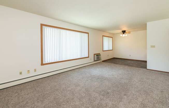 an empty living room with carpet and a large window. Fargo, ND Islander Apartments