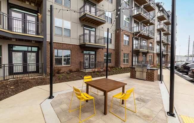 a patio with a table and yellow chairs in front of an apartment building