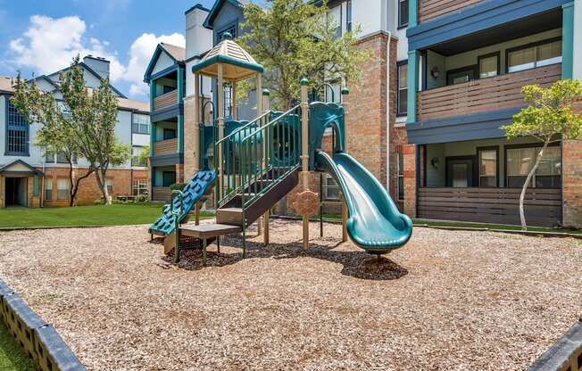 A playground with a green slide and a wooden structure.