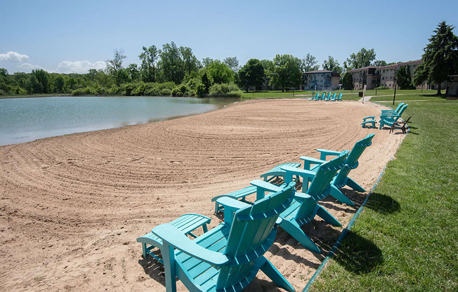 a row of blue beach chairs sitting on the sand near a lake